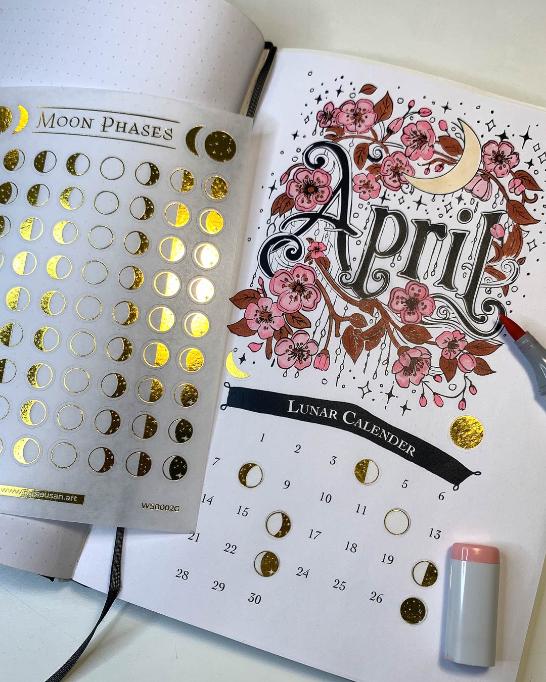 Moon Phase Washi Stickers in gold foil integrated into a handmade April journaling calendar spread, showing lunar phases marked with small 8mm gold stickers on a decorated planner page.