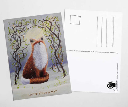 Front and back view of an A6 fox postcard featuring an original oil painting of a red fox in the snow beneath intertwined branches with gold foil keys and fresh green leaves. Gold foil text reads “Light Finds A Way”. The reverse side includes postcard address lines and space for a personal message.