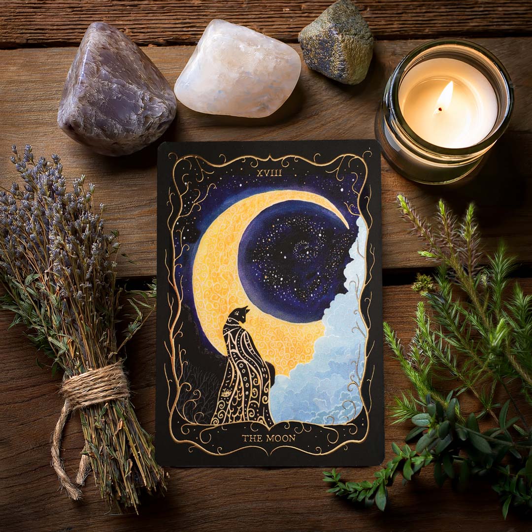 Mystical "The Moon" Tarot postcard with gold foil accents, styled with dried herbs, crystals and candlelight on a rustic wooden surface.