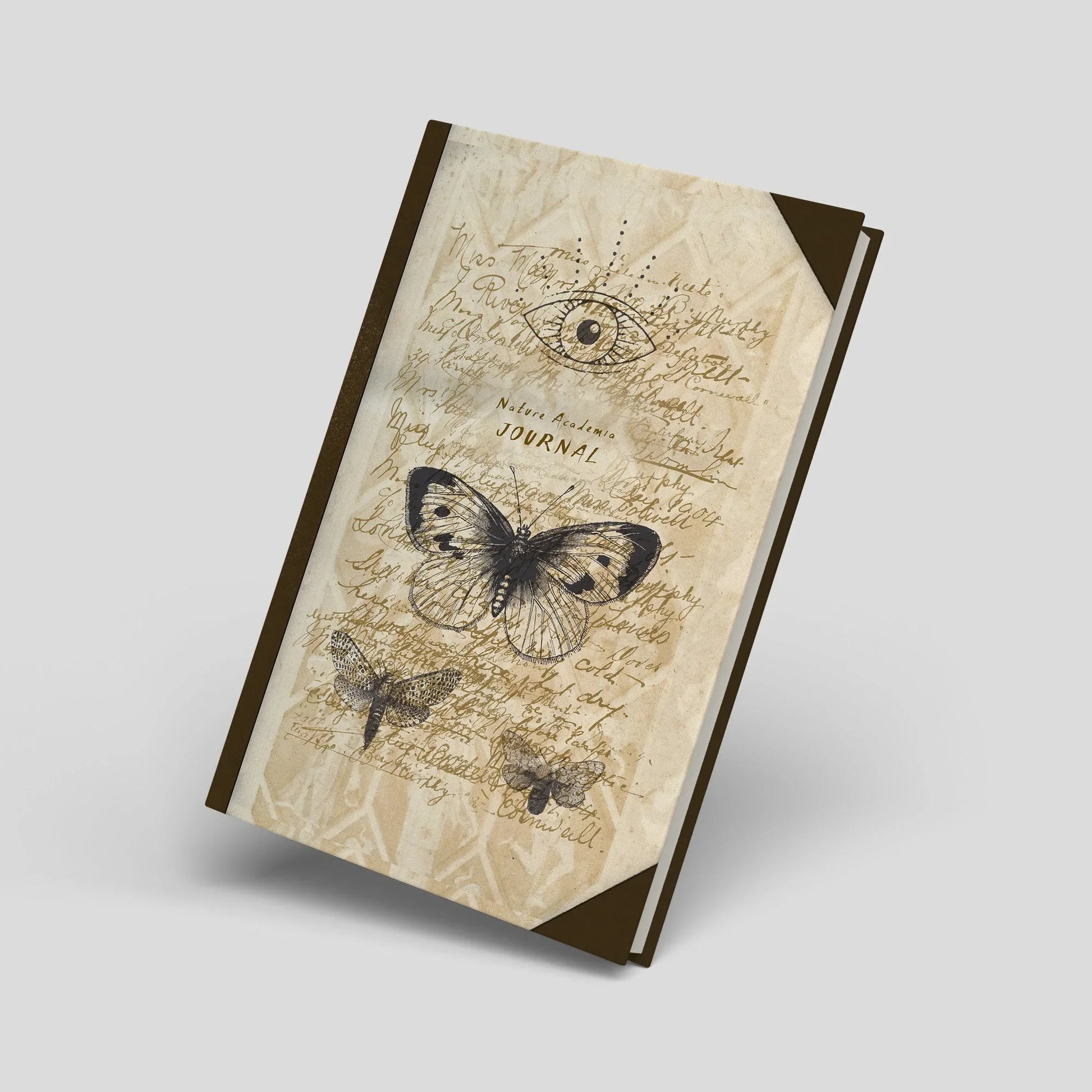 Dark Academia A5 hardcover journal with vintage butterfly and eye design, styled on antique books with a quill, pine cones, fern leaves and natural history inspired objects.