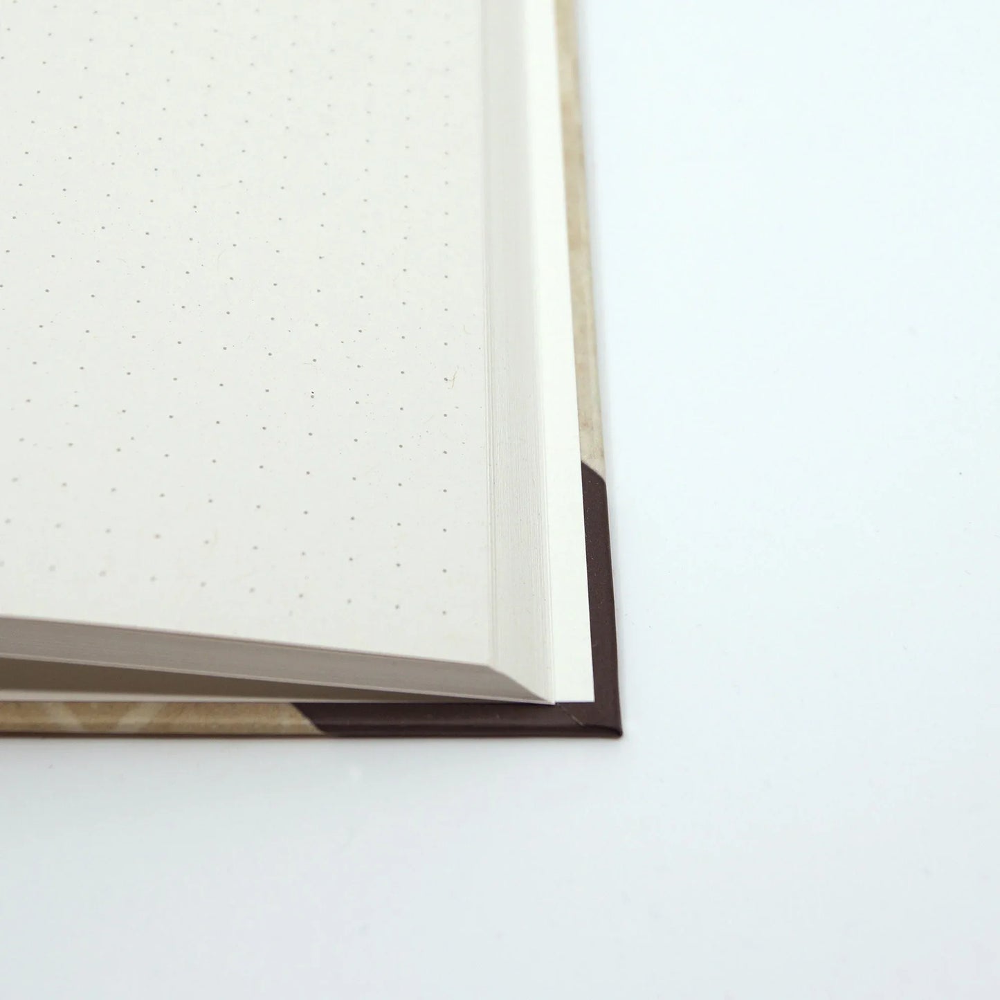 Close-up of the journal opened to reveal the cover corner, sturdy binding and cream coloured recycled paper.