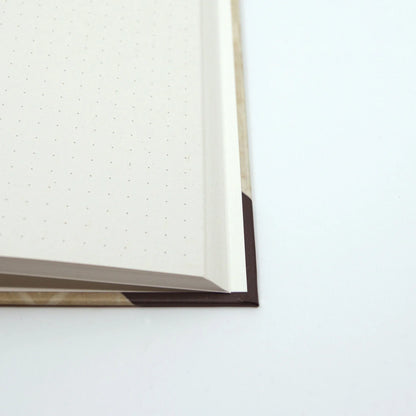 Close-up of the journal opened to reveal the cover corner, sturdy binding and cream coloured recycled paper.