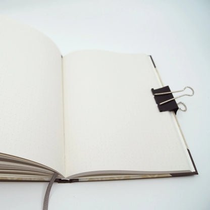Open A5 journal with dot grid pages printed on natural recycled paper, featuring a grey ribbon bookmark and lay-flat hardcover binding.